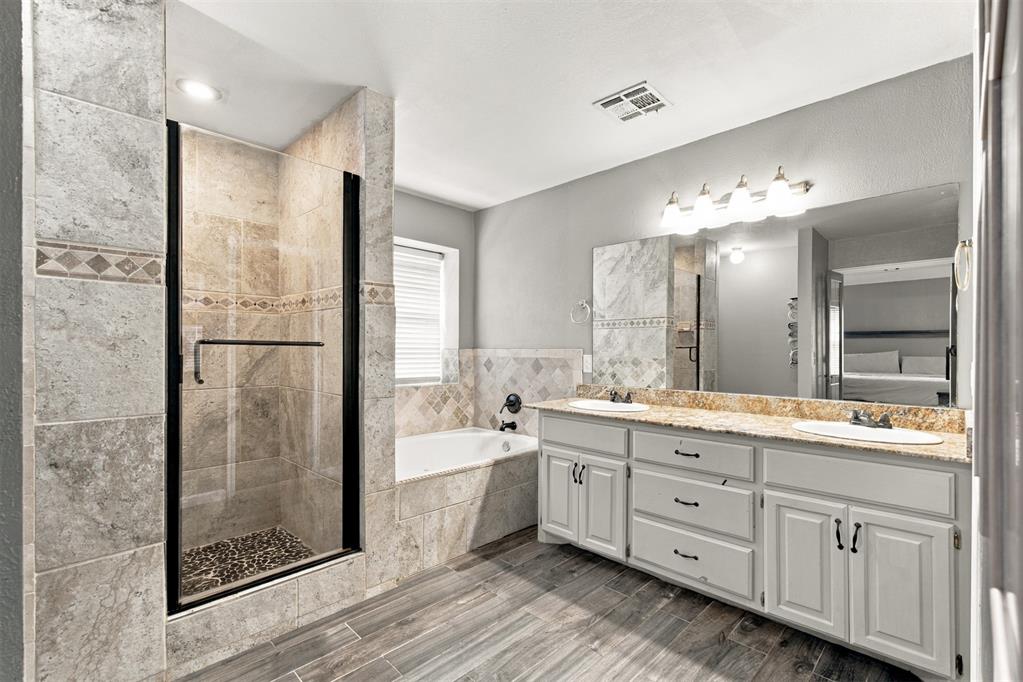 Bathroom with a glass-enclosed tiled shower, bathtub, and long double-sink vanity.