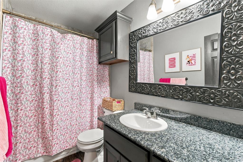 Bathroom with a floral shower curtain, granite vanity, and ornate framed mirror.