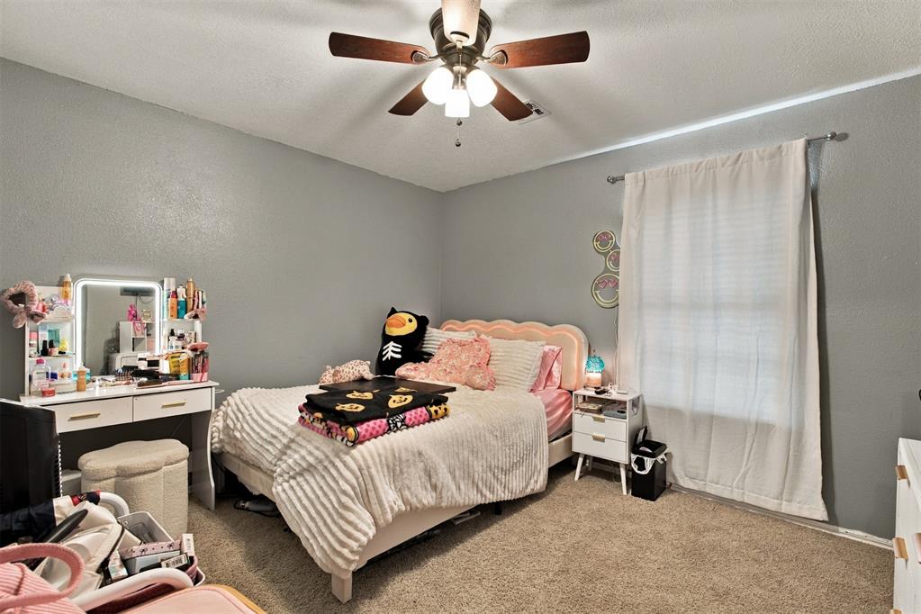 Bedroom with a pink-trimmed bed, vanity, and ceiling fan.