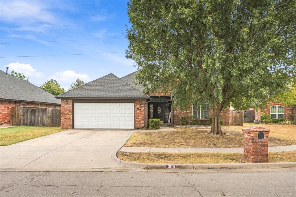 Brick one-story home with an attached garage, broad driveway, and a large front-yard tree.