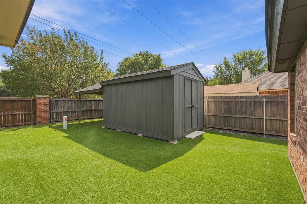 Backyard shed on a green lawn, enclosed by a wooden fence.