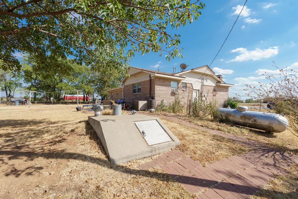 Rear of a brick-and-siding house with a concrete storm cellar entrance and propane tank in the yard.