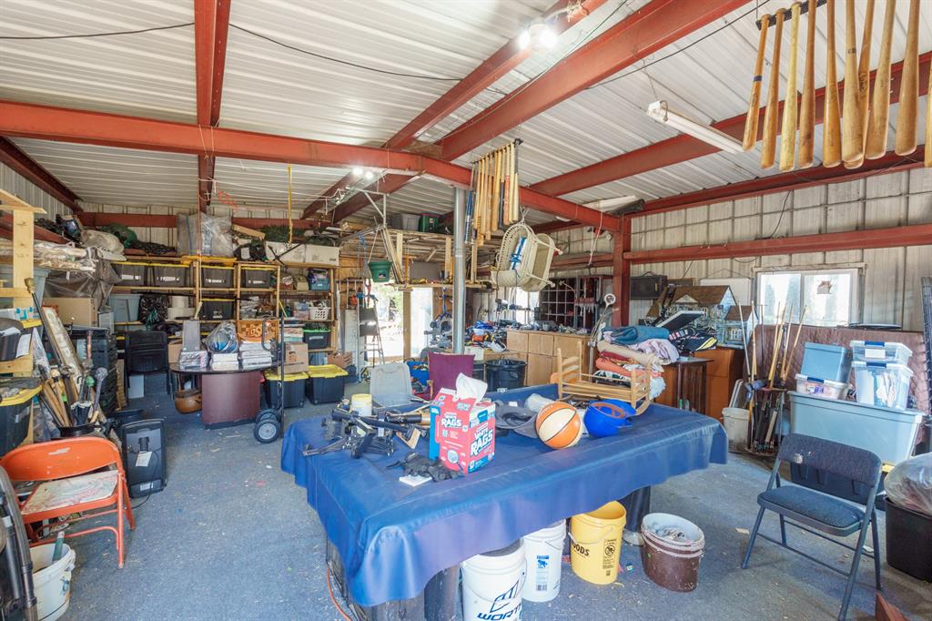 Metal workshop interior with red steel beams, crowded shelving, and a blue-covered worktable.