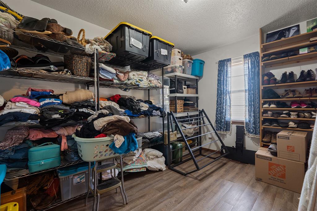Storage room with crowded shelving, clothing, shoes, bins, and a window with blue curtains.