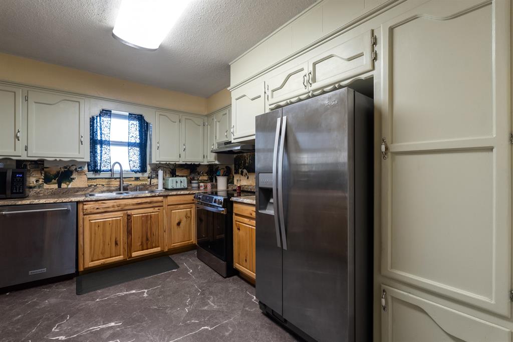 Kitchen with white upper cabinets, wood lower cabinets, stainless steel appliances, and blue curtains over the sink.