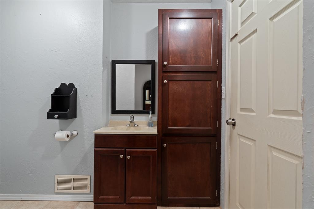 Bathroom vanity with dark wood cabinets, cream countertop, black-framed mirror, and tall storage cabinet.