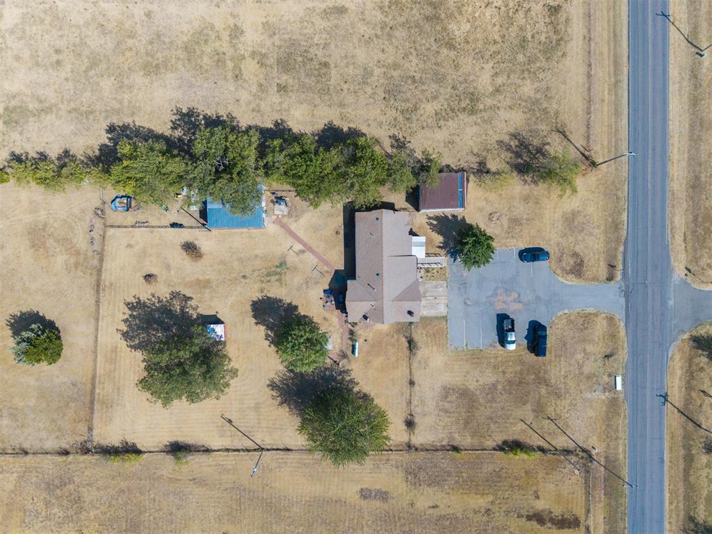 Aerial view of a home on a large grassy lot, with mature trees and paved parking beside the road.