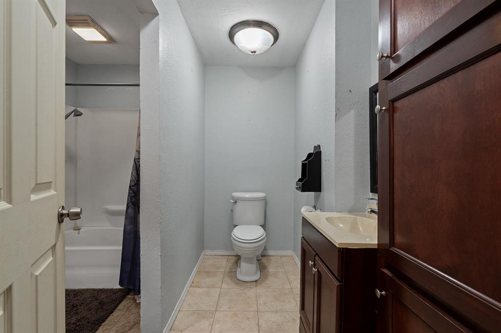 Bathroom with toilet, bathtub and shower, and dark wood vanity with cream countertop.