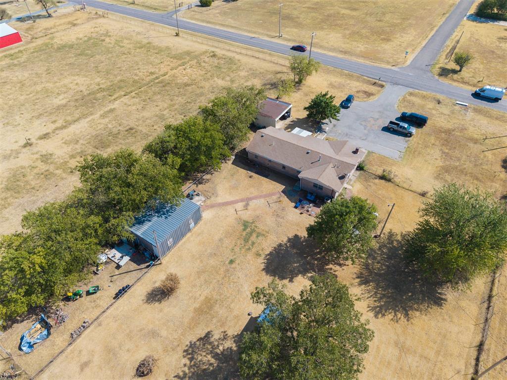 Aerial view of a single-story house, metal outbuilding, and mature trees on a large lot.