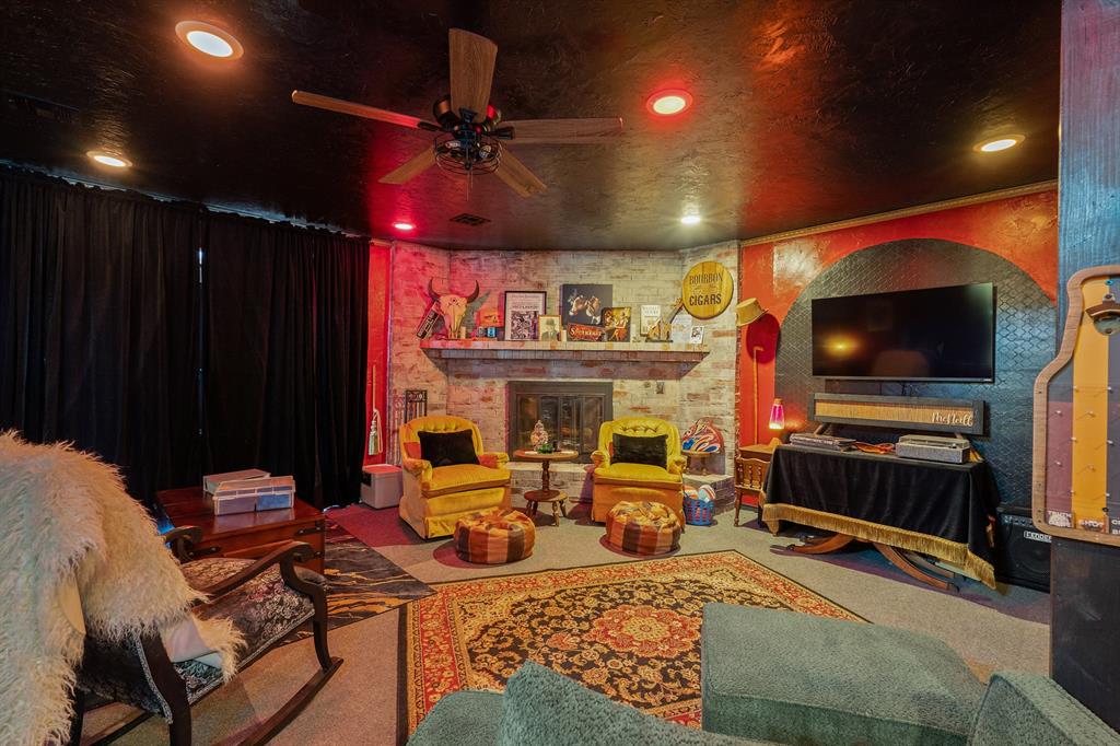Entertainment room with a brick fireplace, yellow armchairs, wall-mounted television, and patterned rugs.
