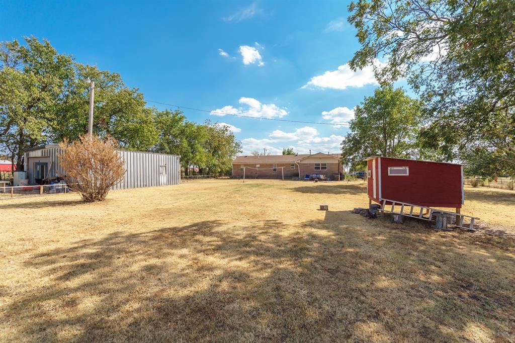 Large dry backyard with a metal outbuilding, red shed, and brick home.