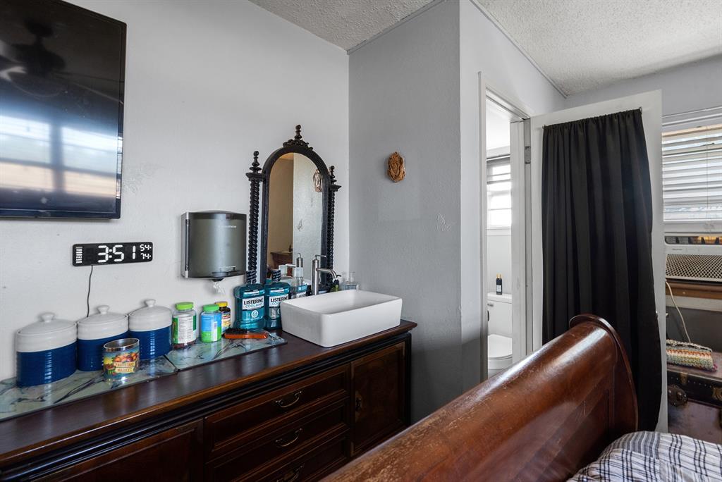 Bedroom with a dark wood dresser, ornate mirror, wall-mounted television, and bathroom doorway.