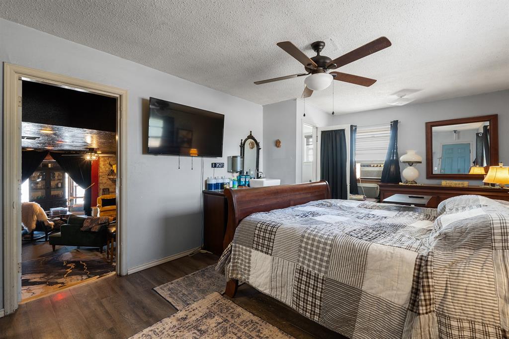 Bedroom with a plaid-covered bed, ceiling fan, wall-mounted television, and doorway to a sitting room.