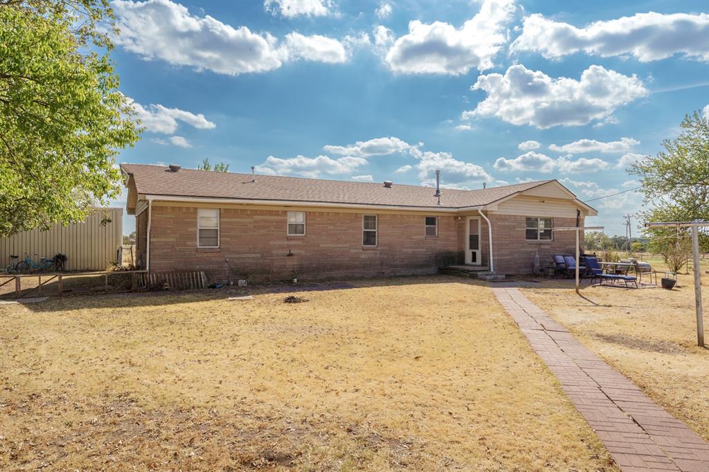 Rear exterior of a single-story brick home with a dry lawn and patio seating.
