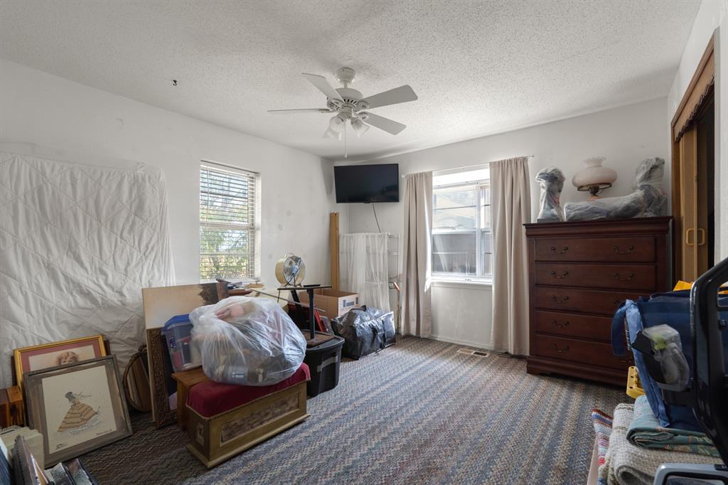 Cluttered bedroom with a wooden dresser, wall-mounted television, and belongings covering the floor.