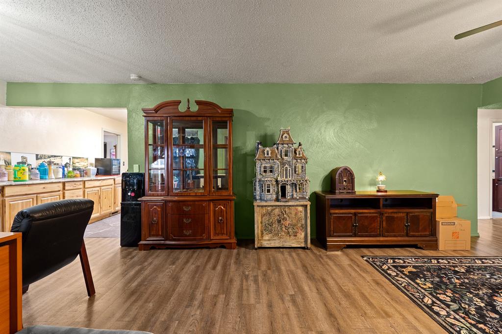 Living room with green wall, wood flooring, dark wood cabinets, and an adjoining kitchen.