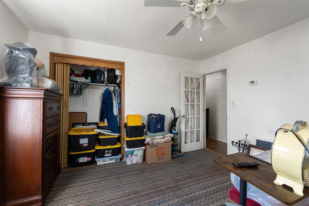 Bedroom with an open, clothing-filled closet, stacked storage bins, and a ceiling fan.