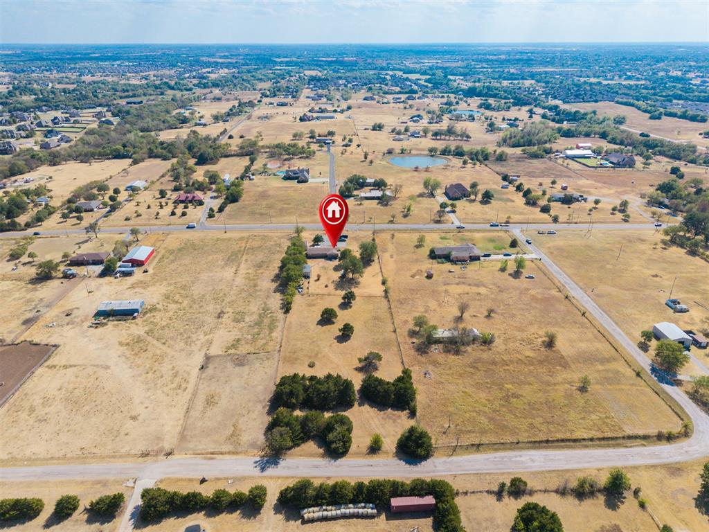 Aerial view of a rural property marked beside a road, surrounded by open fields and scattered homes.