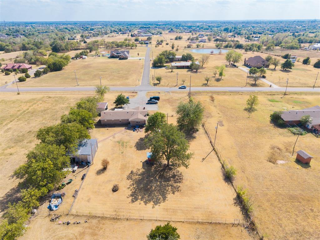 Aerial view of a rural home, outbuildings, and dry fenced acreage beside a road.
