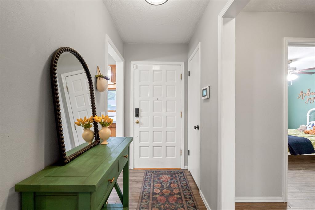 Entry hallway with a green console table, arched mirror, patterned runner, and white paneled front door.