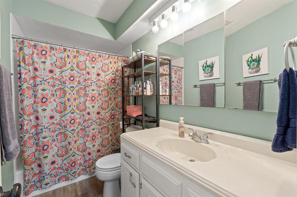 Bathroom with a long white vanity, pale green walls, and a colorful floral shower curtain.