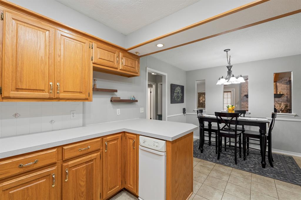 Kitchen with honey-toned wood cabinets and white counters opening to a dining area.