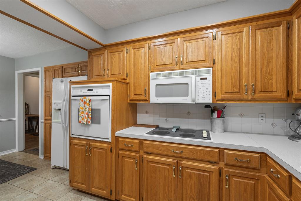Kitchen with honey-colored wood cabinetry, electric cooktop, built-in oven, microwave, and refrigerator.