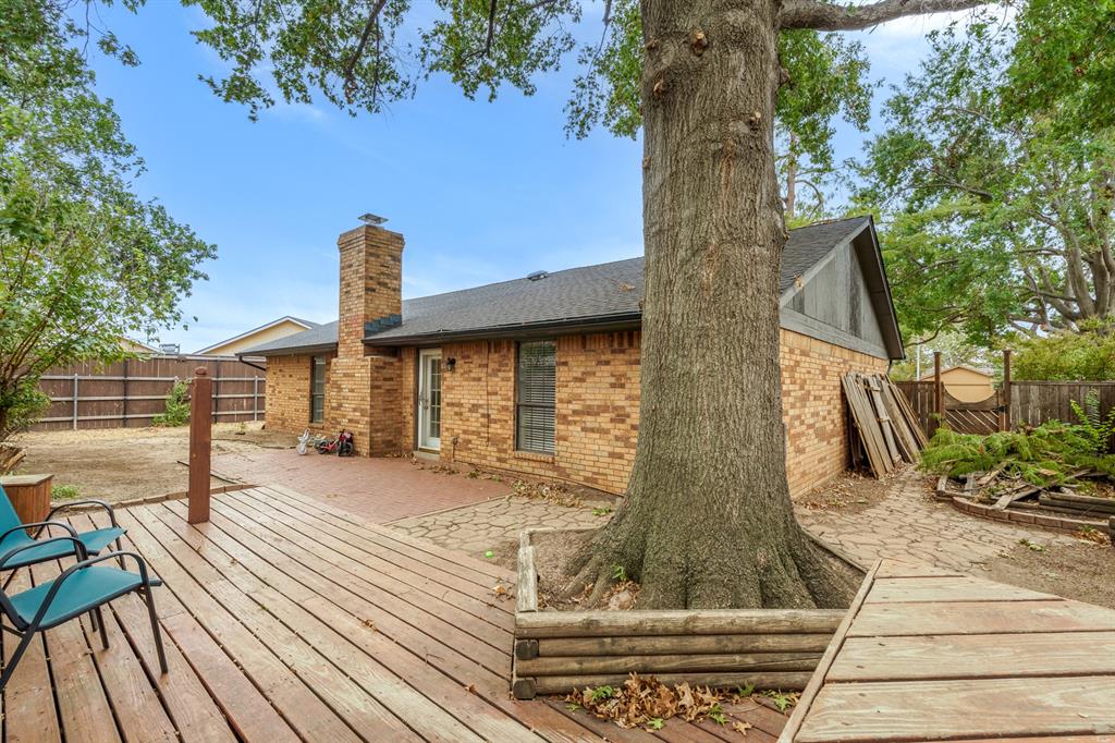 Brick home's backyard with a raised wooden deck, stone patio, and large mature shade tree.