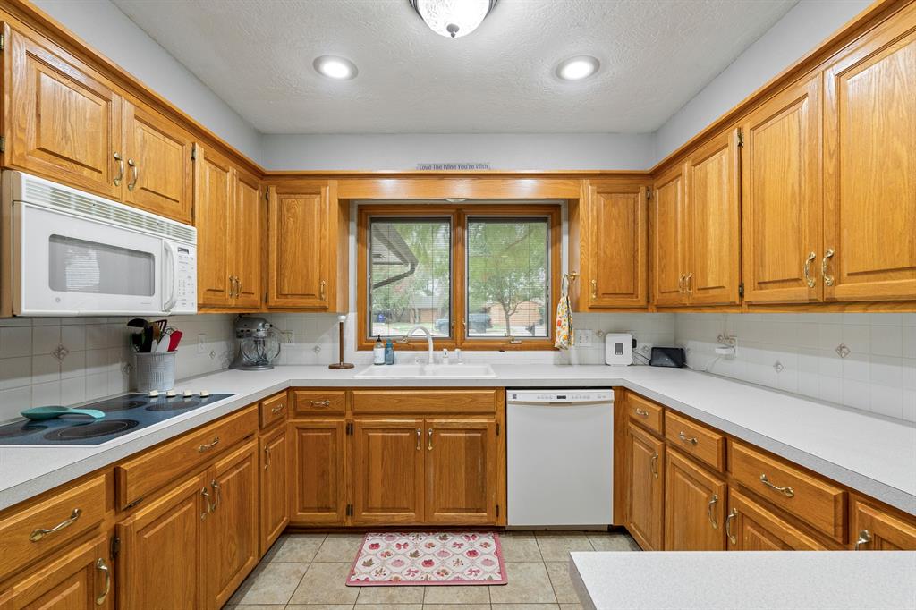 Kitchen with honey-colored wood cabinets, white countertops, and a wide window above the sink.