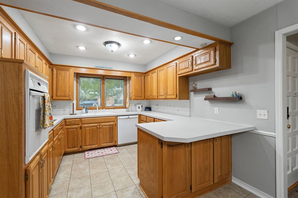 Kitchen with honey-toned wood cabinets, white countertops, and a peninsula beside the sink window.