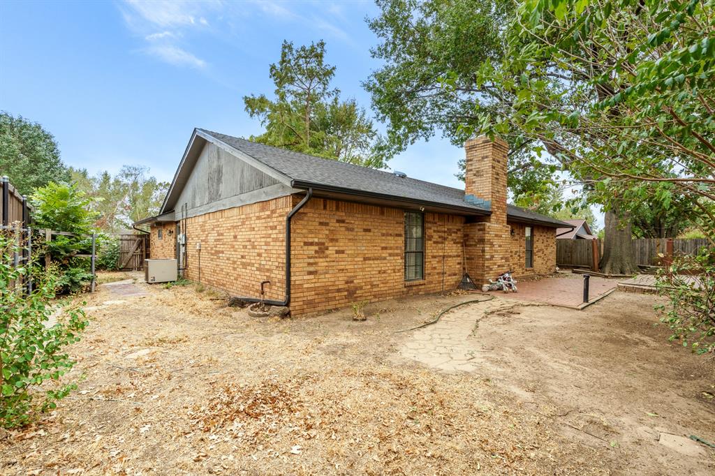 Brick home’s rear exterior with a gabled roof, chimney, and fenced backyard patio.