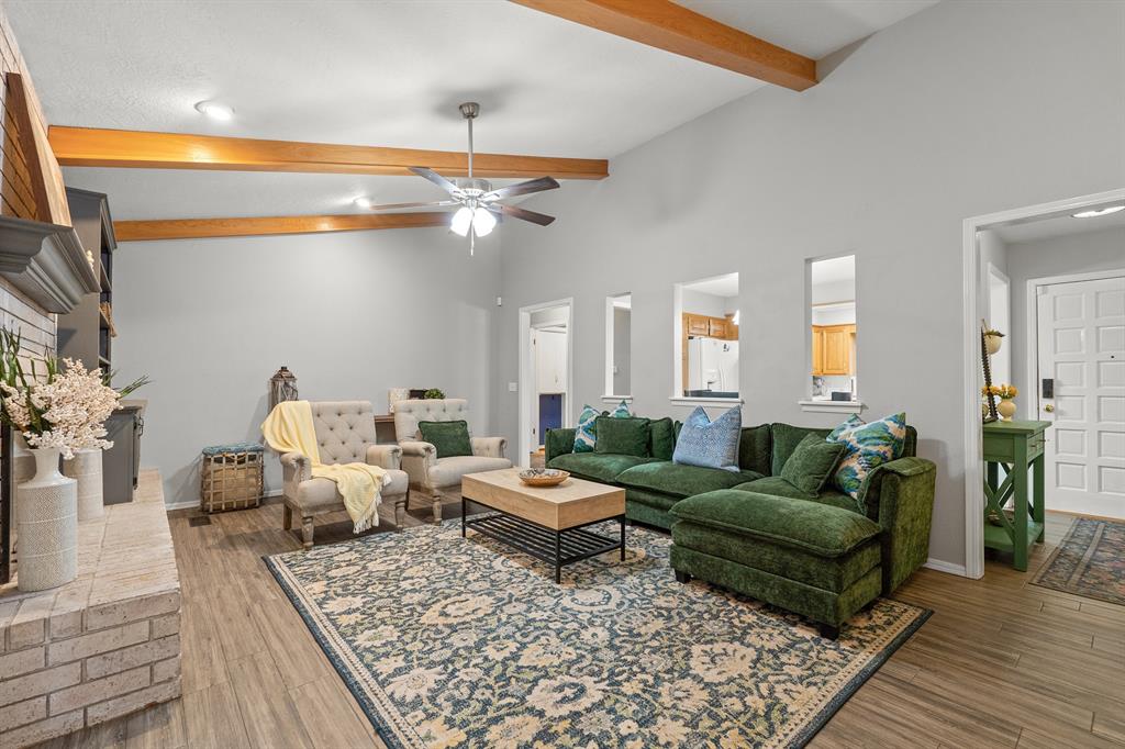 Living room with a green sectional, patterned rug, and exposed wood ceiling beams.
