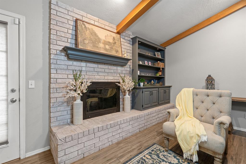 Living room with a whitewashed brick fireplace, dark built-ins, exposed wood beams, and a chair with a yellow throw.
