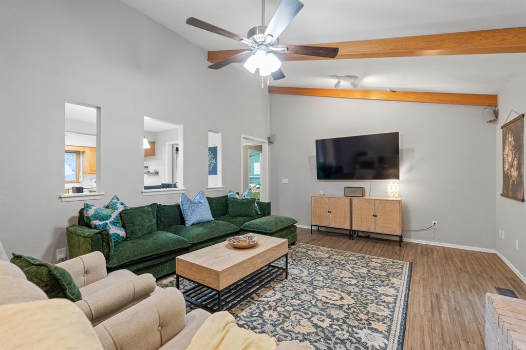 Living room with a green sectional, patterned rug, wall-mounted television, and wood ceiling beams.