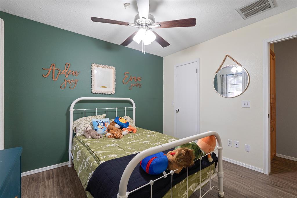 Bedroom with a green accent wall, white metal bed, floral bedding, and stuffed animals.