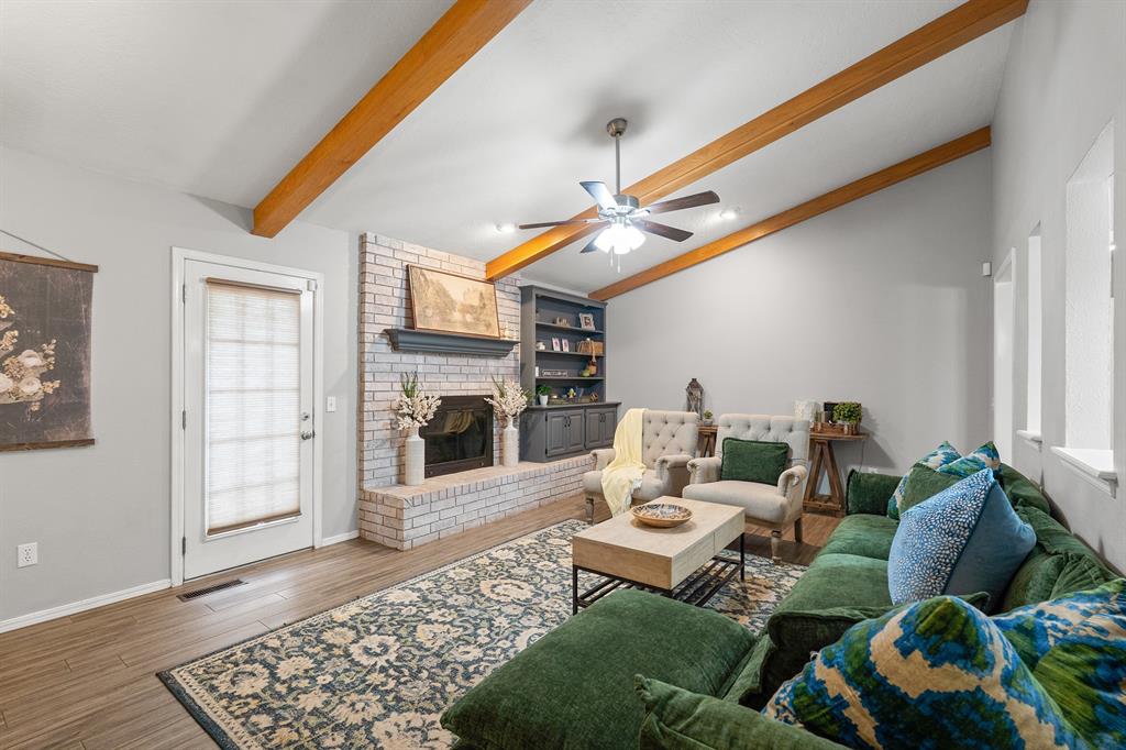 Living room with a white brick fireplace, exposed wood beams, and a green sectional sofa.