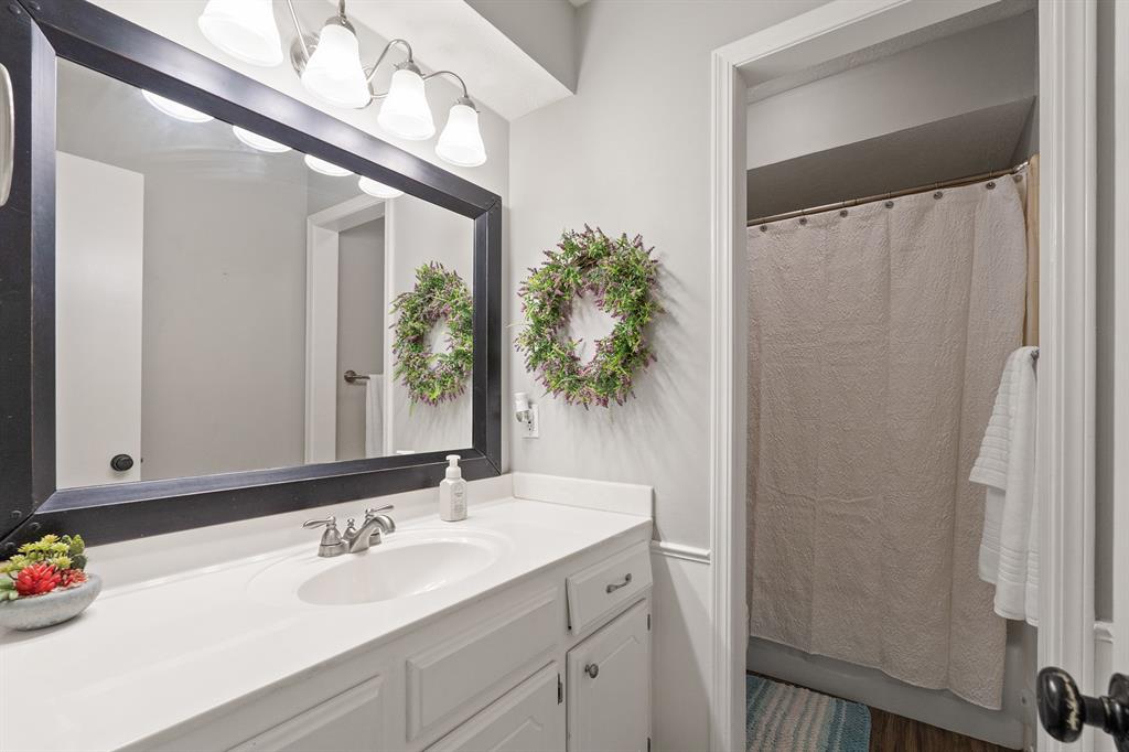 Bathroom with a white vanity and large dark-framed mirror beside a curtained shower.
