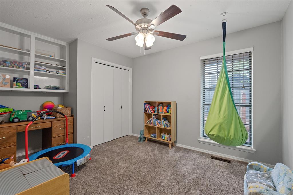 Children's playroom with built-in shelves, a small trampoline, and a green hanging chair by the window.