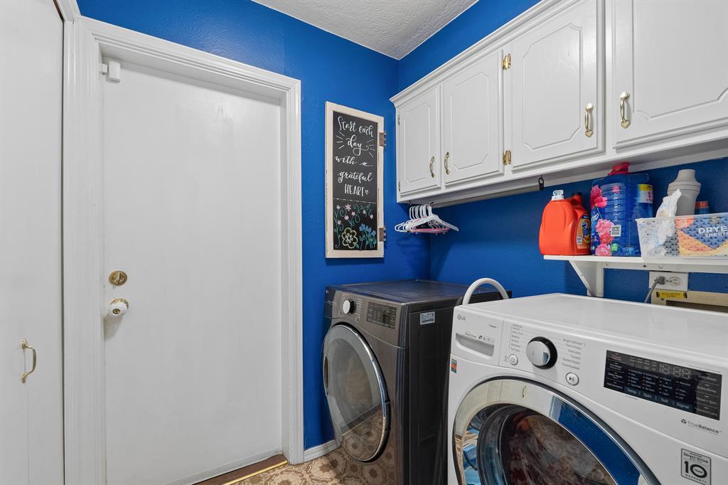 Laundry room with blue walls, white cabinets, and front-loading washer and dryer.