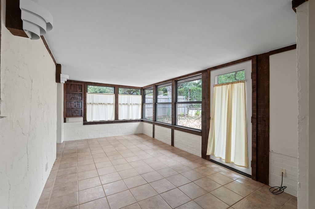 Empty sunroom with a tiled floor, dark wood window framing, and a curtained glass door.