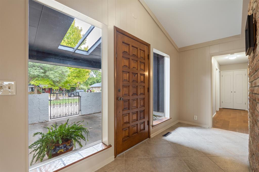 Entryway with a paneled wooden front door, tall patio-facing windows, tiled floor, and brick accent wall.