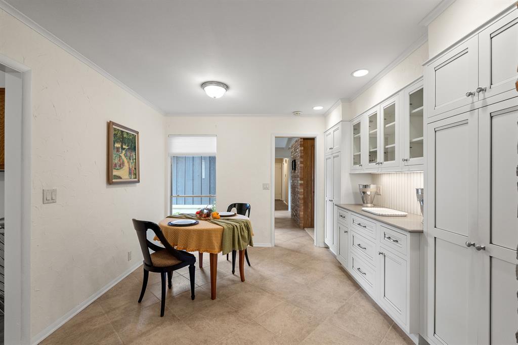 Kitchen with white cabinetry and a small dining table set beneath a window.