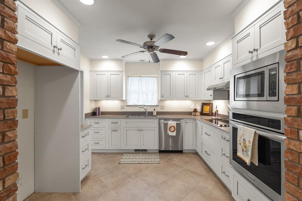 Bright kitchen with white cabinets, stainless steel appliances, dark countertops, and brick doorway edges.