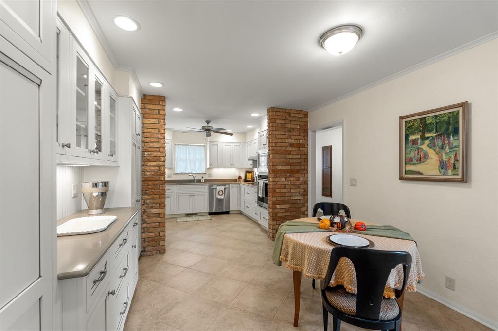 Kitchen and dining area with white cabinets, exposed brick columns, and a set dining table.