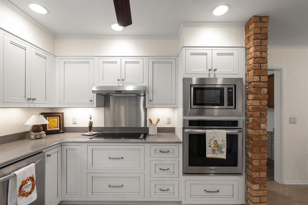 Kitchen with white paneled cabinets, gray counters, stainless steel appliances, and a brick column.
