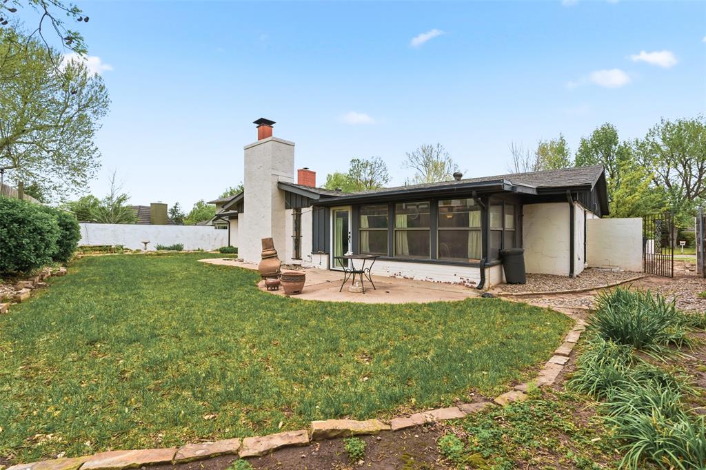 Rear of a single-story home with a screened porch, tall chimney, and grassy backyard.