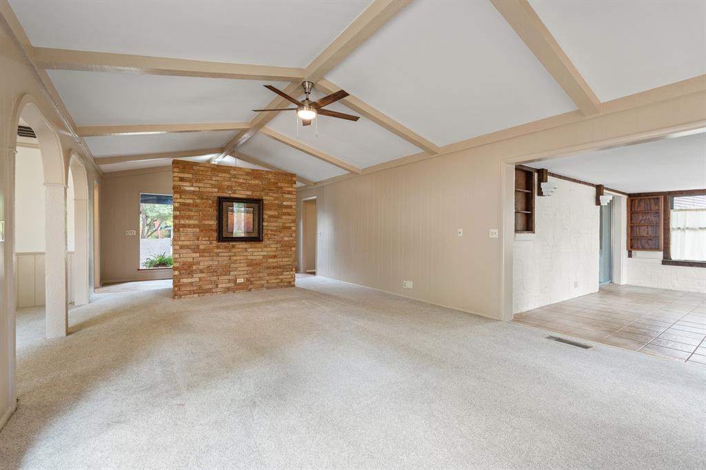 Empty living room with vaulted beamed ceiling, light carpet, and brick partition.