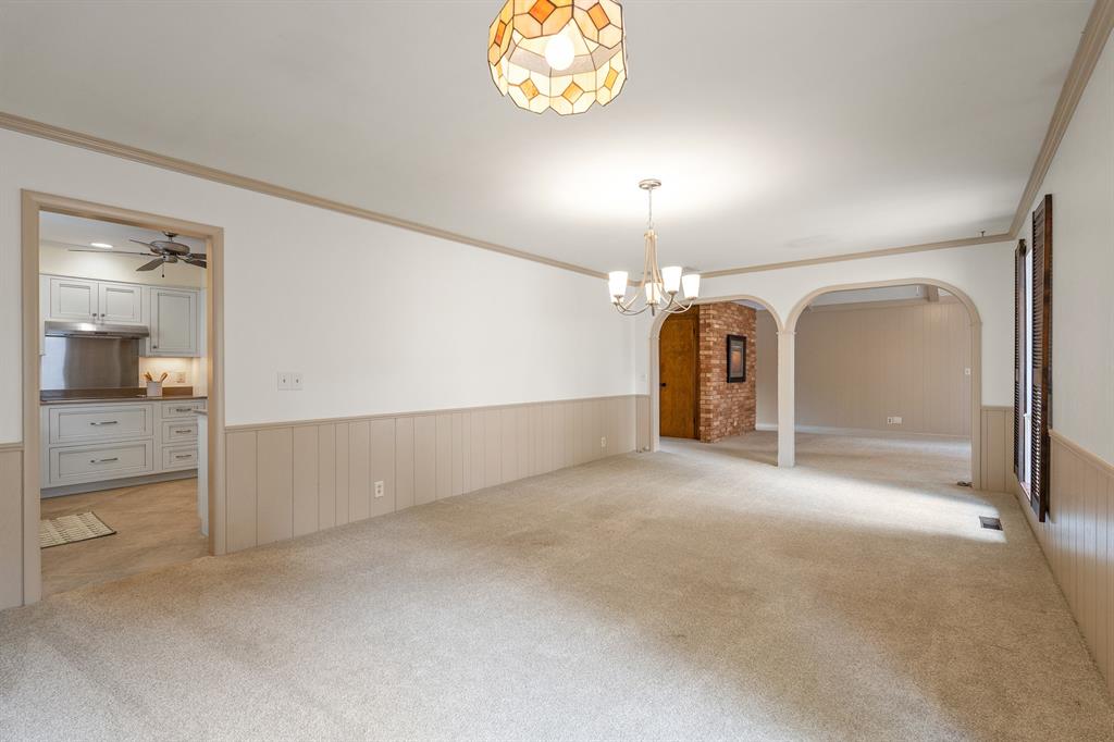 Empty carpeted dining room with paneled walls, a chandelier, and arched openings to adjoining rooms.