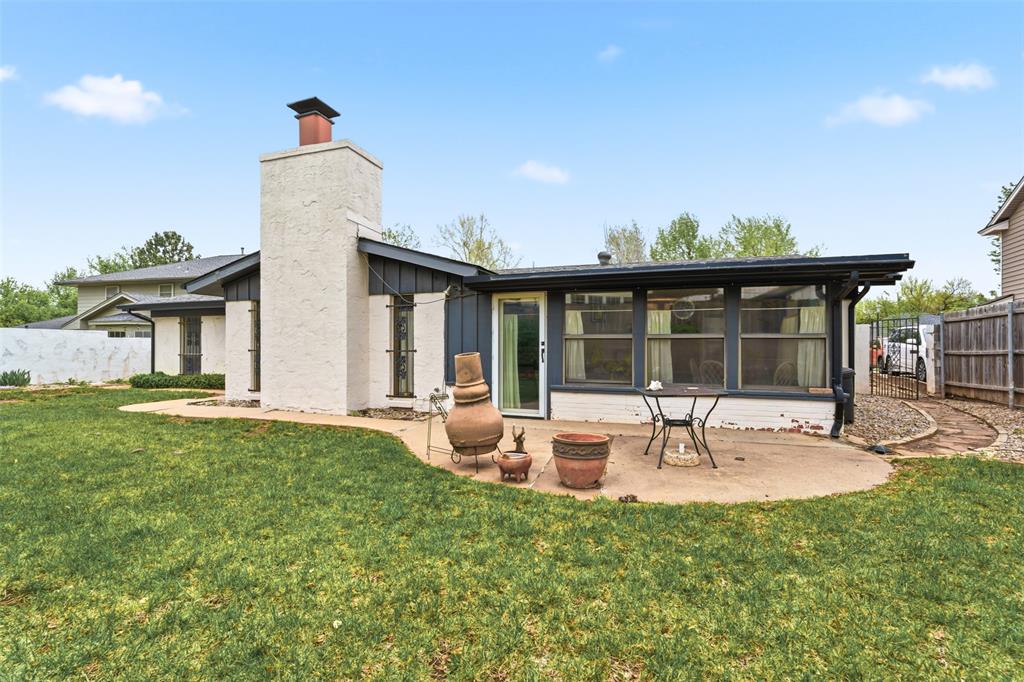 Rear of a single-story home with a tall white chimney, sunroom windows, and a patio with planters.