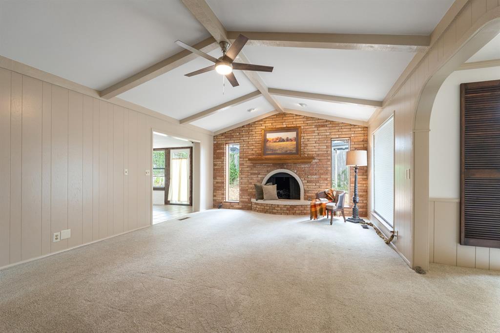 Living room with a vaulted beamed ceiling, brick fireplace, and beige carpet.